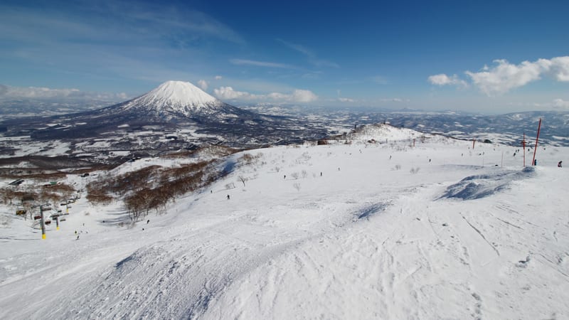 Skiers on a wide snow-covered piste at Niseko Grand Hirafu with the cone of Mount Yotei behind, Hokkaido in midwinter