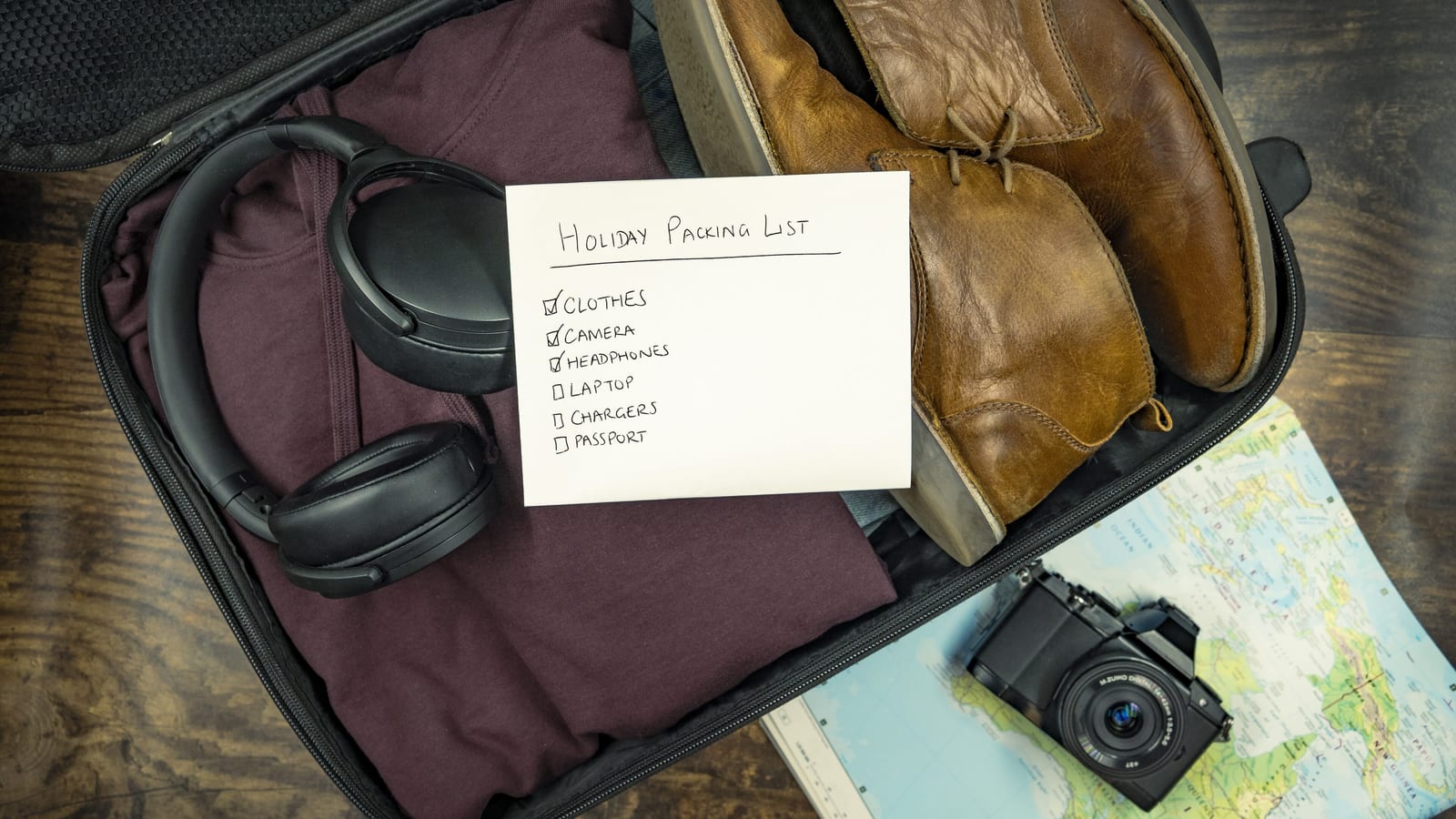Open suitcase with a handwritten packing list, headphones, camera and chargers ready for an overseas trip
