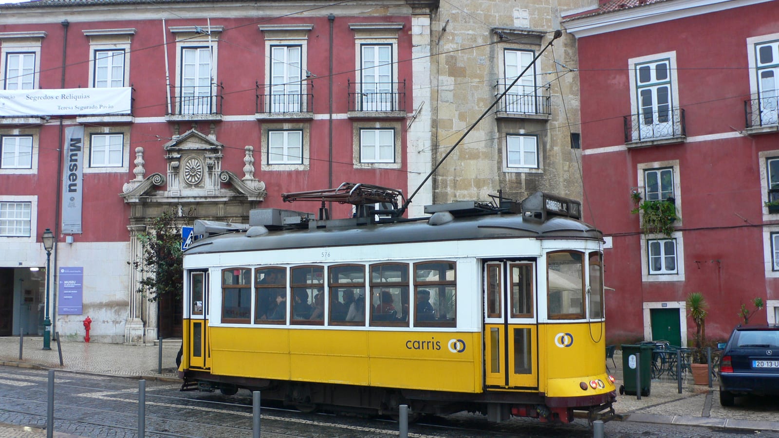 A yellow tram climbing a street below Sao Jorge Castle, Lisbon, Portugal